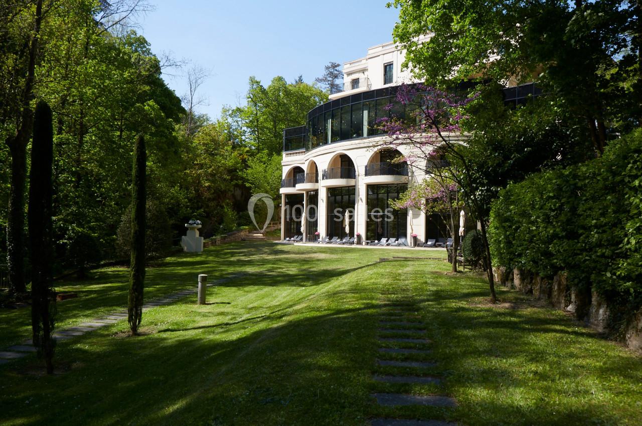 Façade d'un bâtiment moderne entouré de verdure, avec une pelouse et des arbres sous un ciel dégagé.