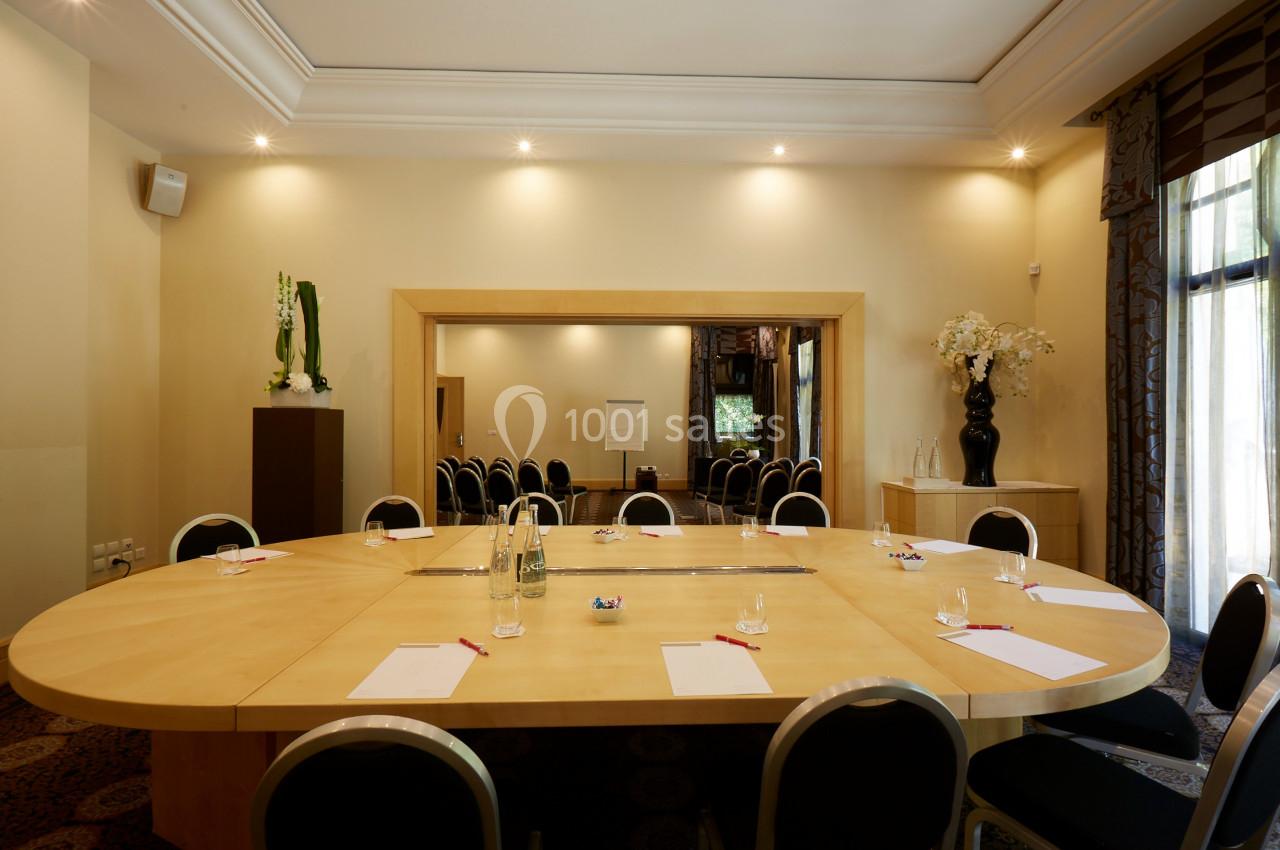 Salle de réunion lumineuse avec une grande table ovale, des chaises noires et des fournitures disposées.