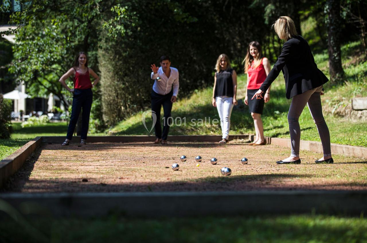 Des personnes jouent à la pétanque sur un terrain en plein air, entouré de verdure.