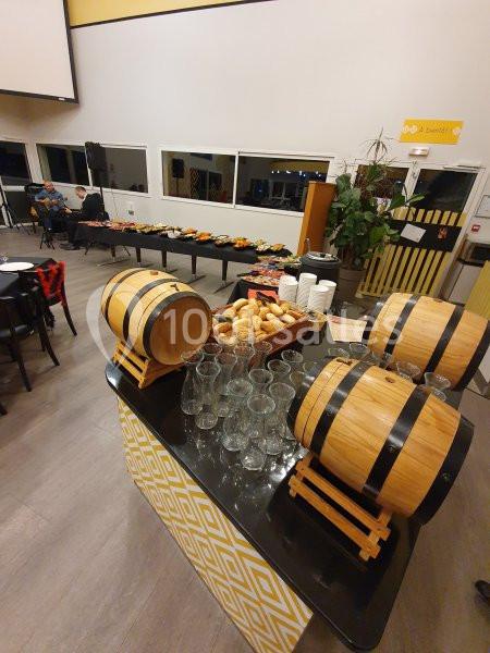 Buffet avec tonneaux en bois, verres, paniers de pain et plats disposés sur des tables dans une salle lumineuse.