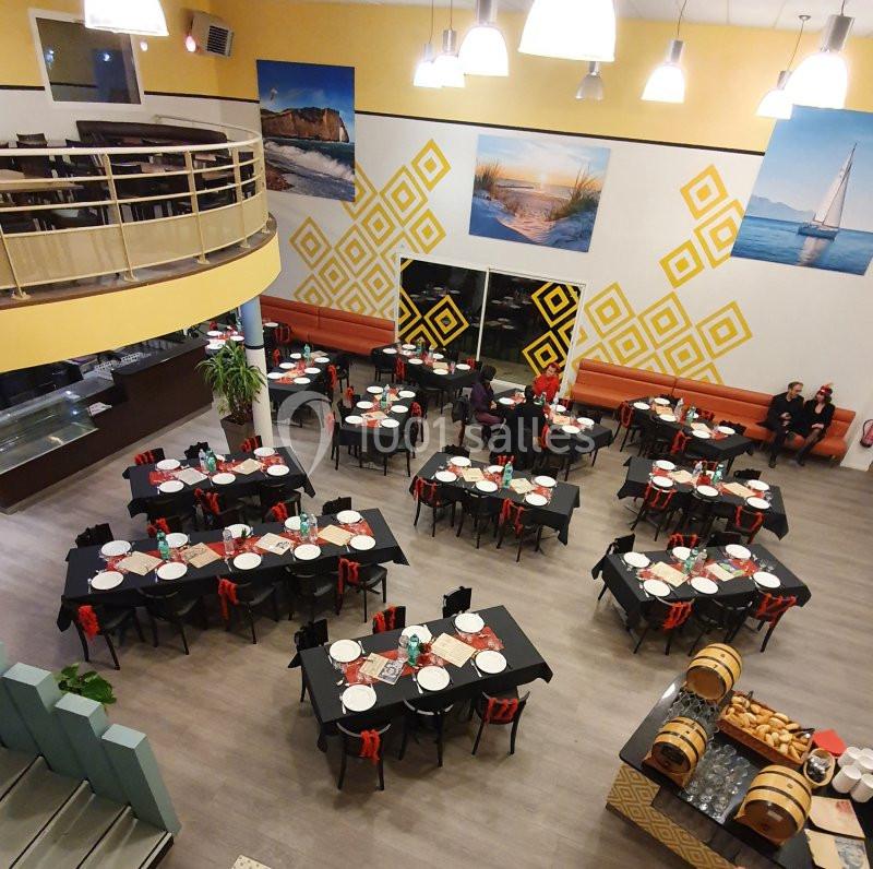 Salle de restaurant spacieuse avec tables dressées en noir et rouge, décor mural nautique et mezzanine visible.