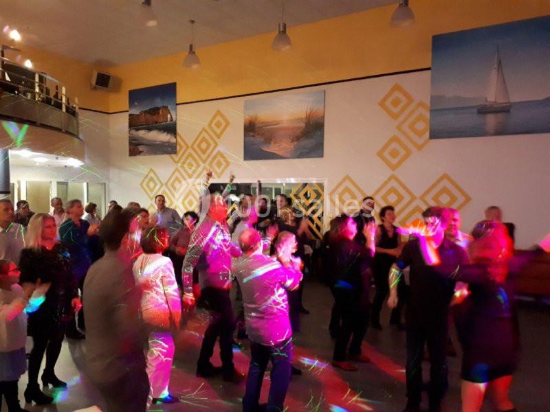 Groupe de personnes dans une salle illuminée par des jeux de lumière, dansant ou discutant lors d'un événement festif.