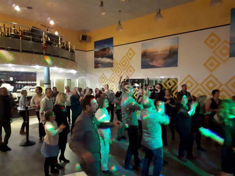 Groupe de personnes dans une salle, dansant sous des lumières colorées, avec une décoration murale géométrique.