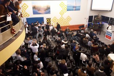 Miniature Location salle Saint-Contest (Calvados) - L'Essentiel #18 Salle comble avec des participants assis et debout lors d'un événement, décorée avec un sapin de Noël et des tableaux muraux.