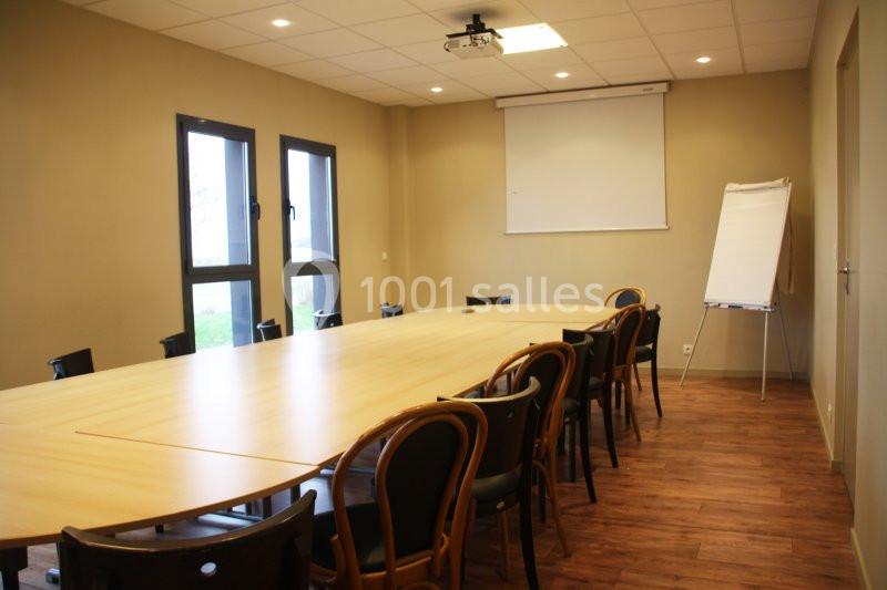 Salle de réunion avec une grande table en bois, des chaises, un tableau blanc et un vidéoprojecteur au plafond.