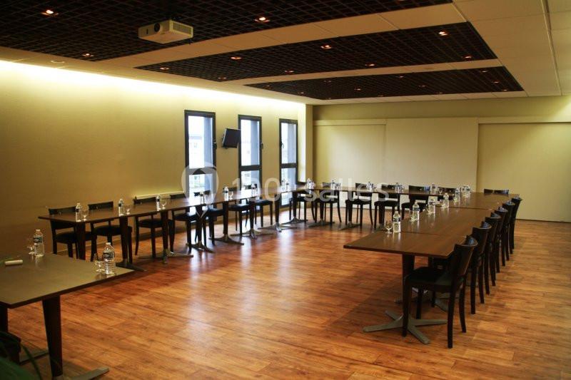 Salle de réunion avec tables disposées en U, chaises alignées et bouteilles d'eau sur chaque table.