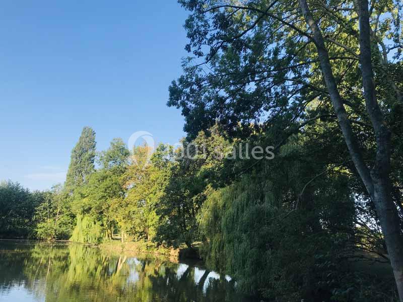 Vue d'un étang entouré d'arbres verdoyants sous un ciel bleu clair.