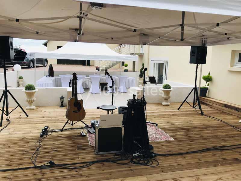 Scène extérieure équipée d'instruments de musique et de matériel audio sous des tentes blanches sur une terrasse en bois.