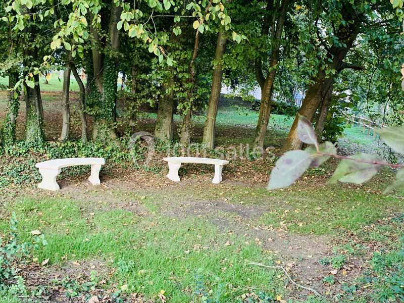 Deux bancs en pierre disposés sur une pelouse, entourés d'arbres et de feuillage dans un cadre naturel.