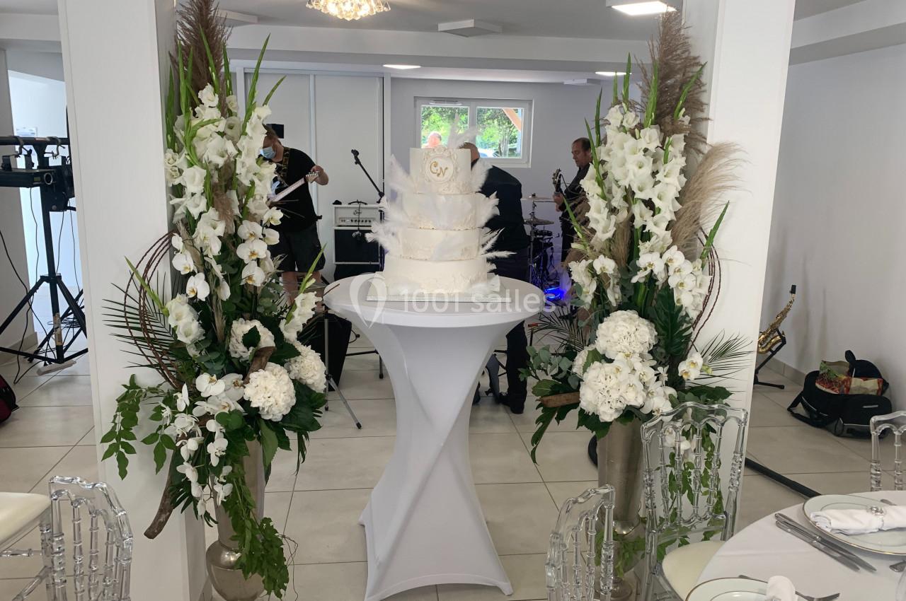 Gâteau de mariage blanc à plusieurs étages sur une table, entouré de grandes compositions florales blanches.