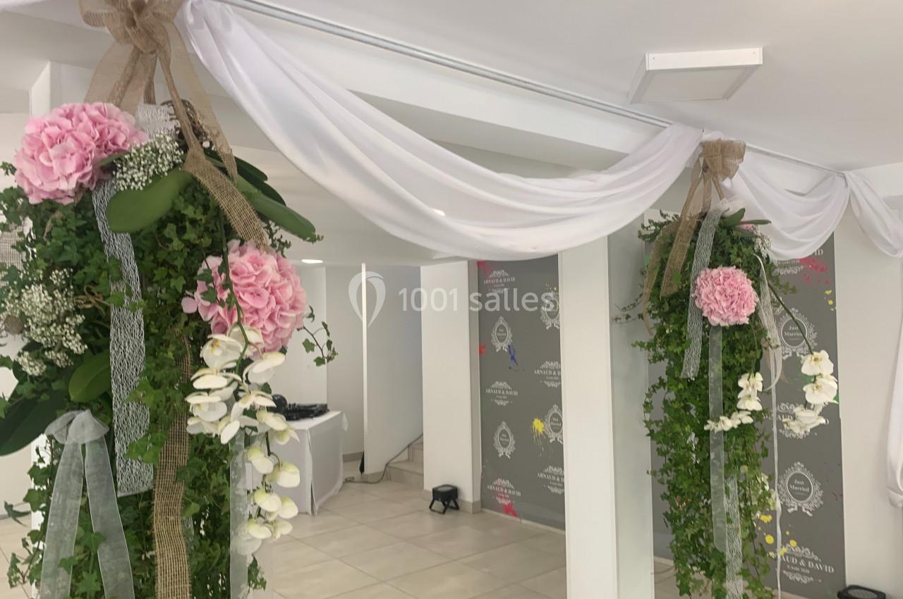 Décoration florale suspendue avec des drapés blancs, des fleurs roses et blanches, et du feuillage dans une salle lumineuse.