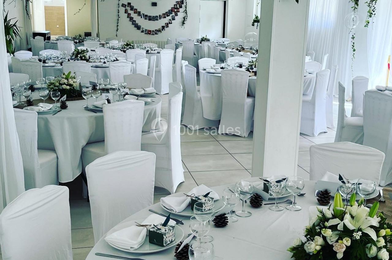 Salle de réception décorée avec des tables rondes, nappes blanches, centres de table floraux et guirlandes végétales.