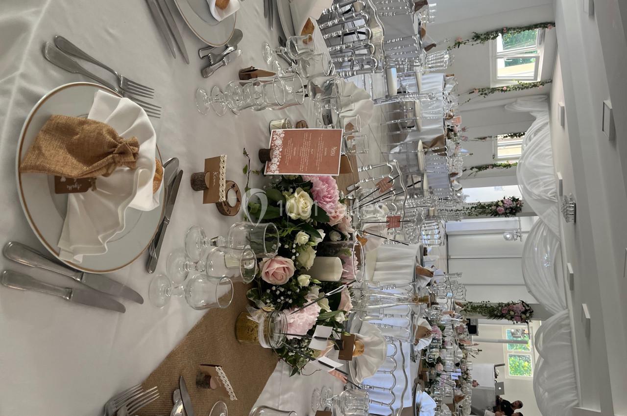 Table de réception élégamment dressée avec nappes blanches, vaisselle raffinée, centre de table floral et décoration…