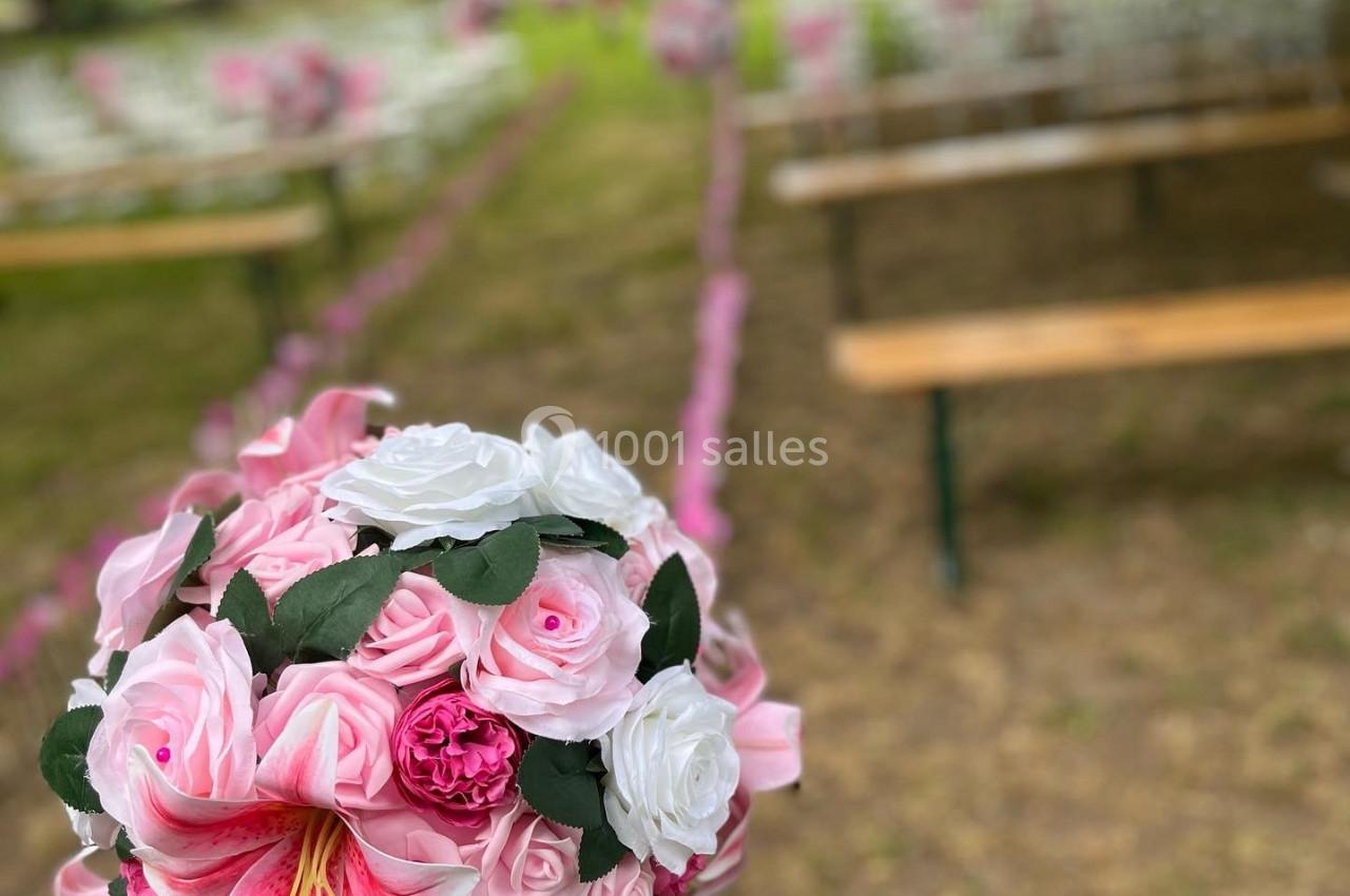 Bouquet de fleurs roses et blanches au premier plan, avec des bancs alignés dans un jardin en arrière-plan.