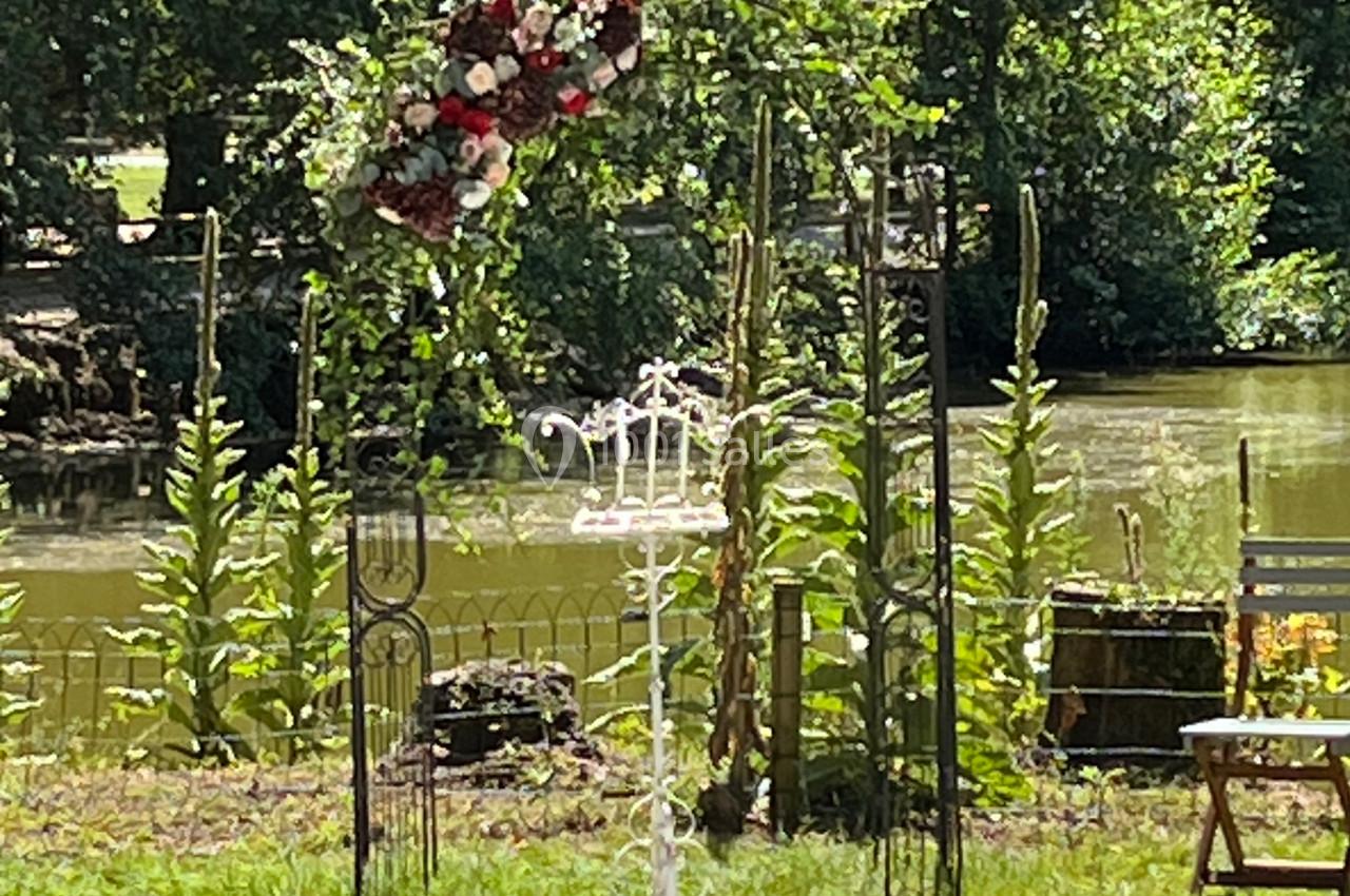 Arche fleurie et allée blanche installées en extérieur près d'une rivière pour une cérémonie.