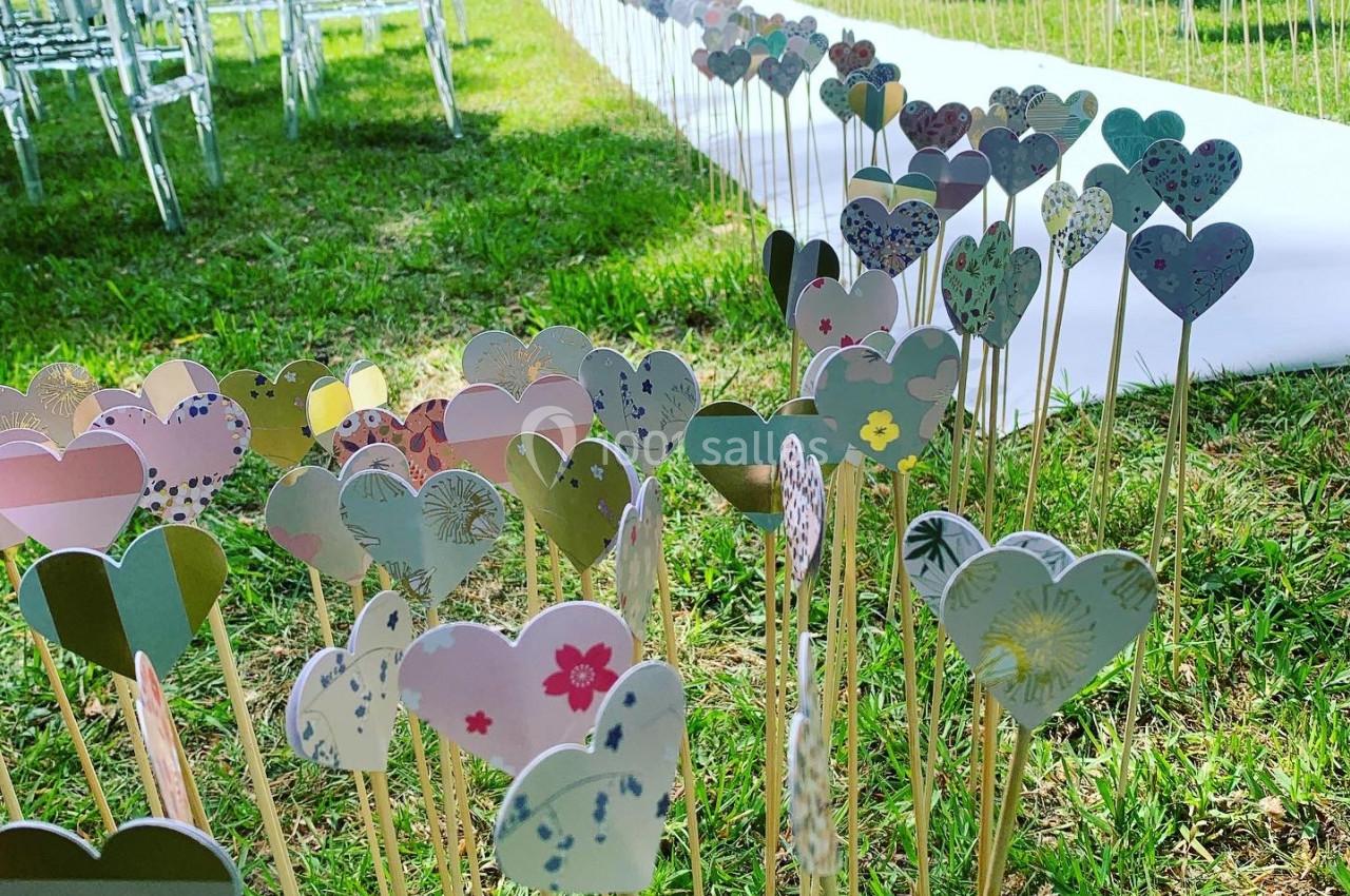 Cœurs en papier colorés plantés sur des tiges dans l'herbe, décorant une allée pour une cérémonie en plein air.
