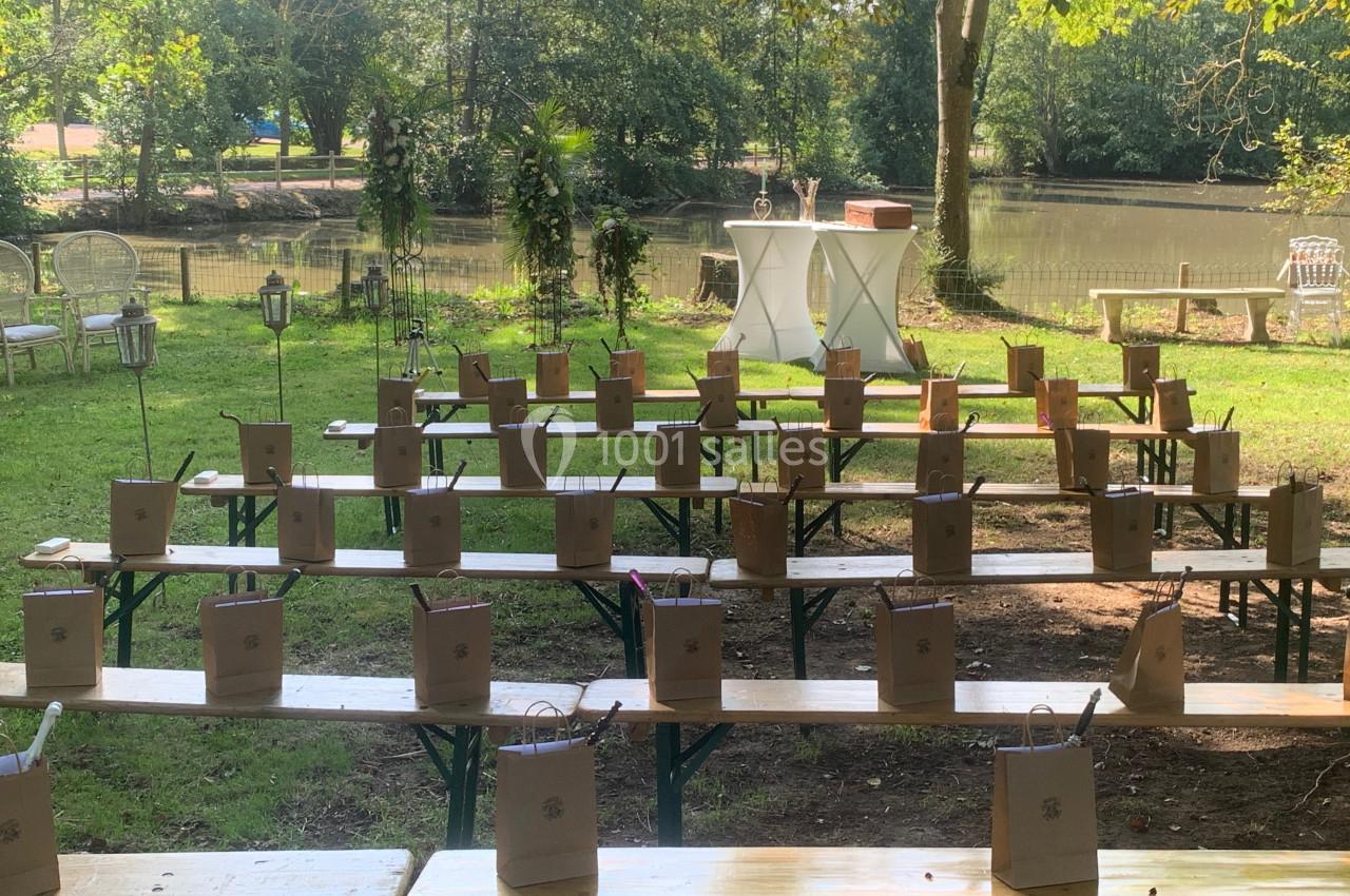 Bancs en bois disposés en extérieur, ornés de sacs en papier, avec une table blanche en arrière-plan près d'un étang.