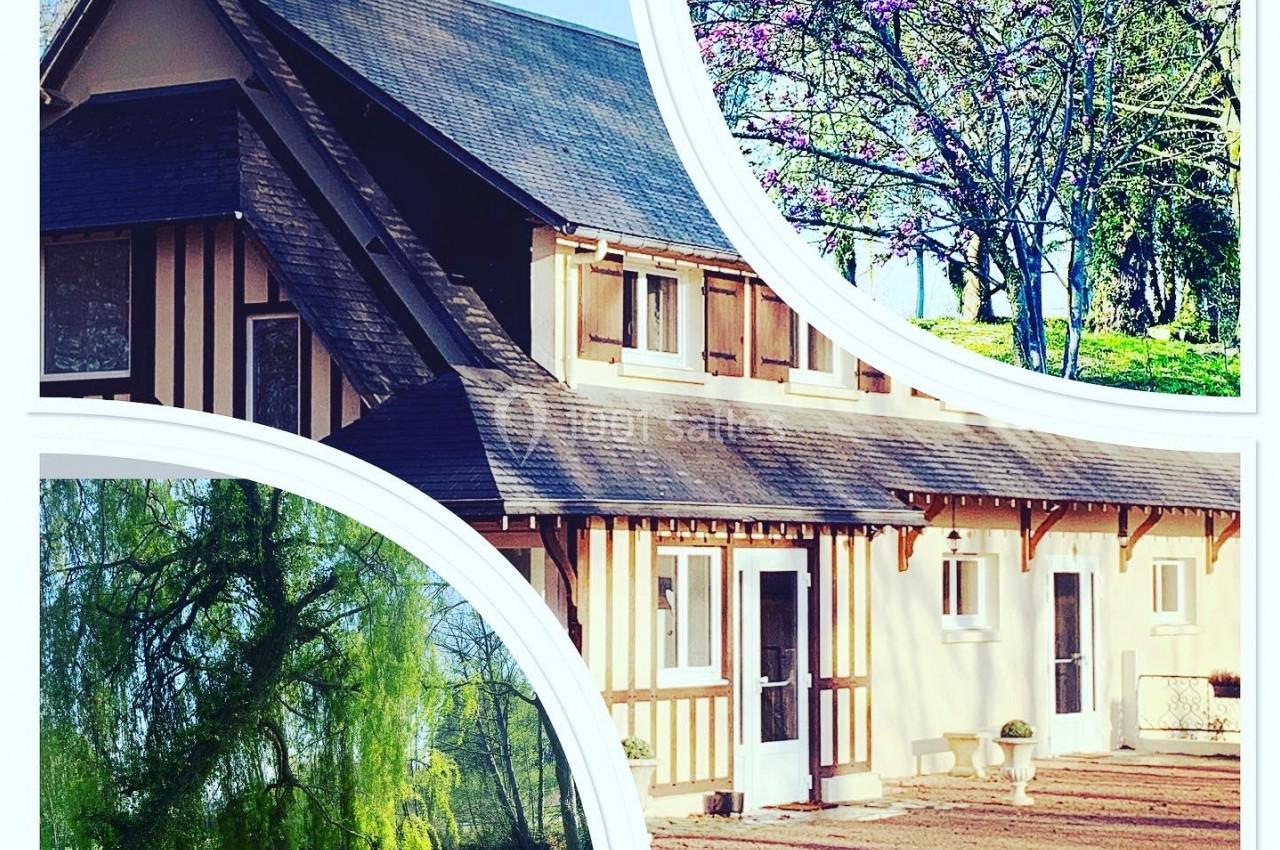 Maison à colombages avec toit en ardoise, entourée d'arbres fleuris et d'un grand jardin verdoyant.