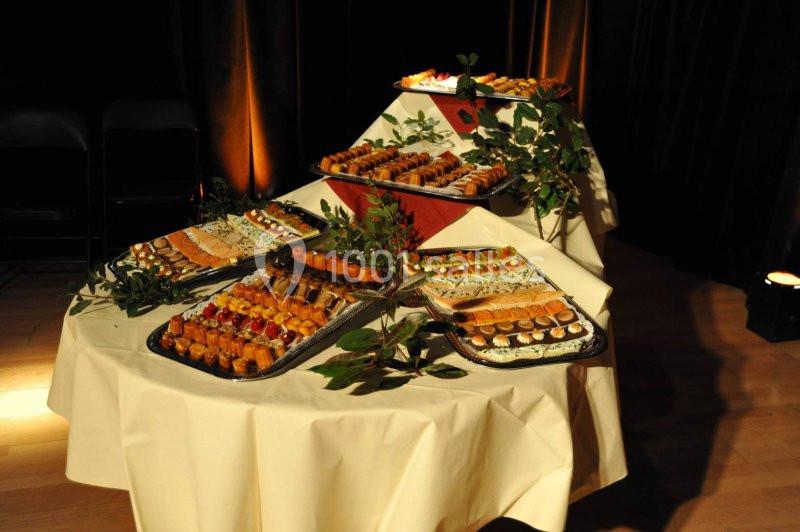 Plateaux de petits fours variés disposés sur une table ronde, décorée de feuillage, dans une ambiance tamisée.