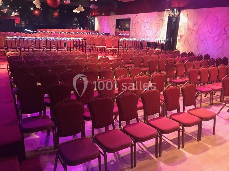 Salle de spectacle avec rangées de chaises rouges alignées, éclairage tamisé et décorations murales.