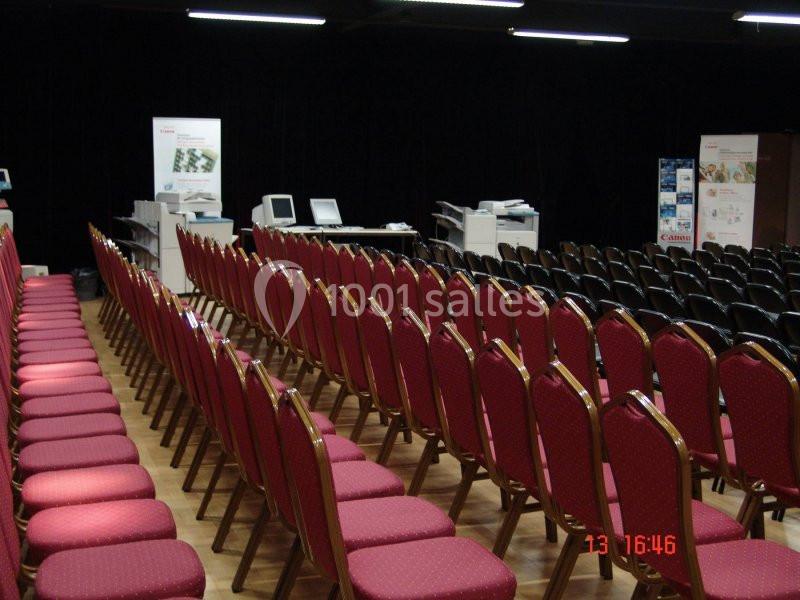 Rangées de chaises rouges alignées dans une salle avec des équipements informatiques en arrière-plan.