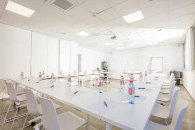 Quatre fauteuils noirs avec coussins clairs entourent une table basse dans une pièce décorée de cadres et luminaires…