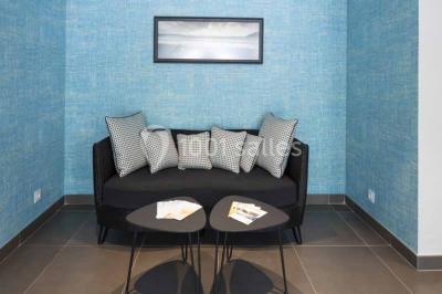 Quatre fauteuils noirs avec coussins clairs entourent une table basse dans une pièce décorée de cadres et luminaires…