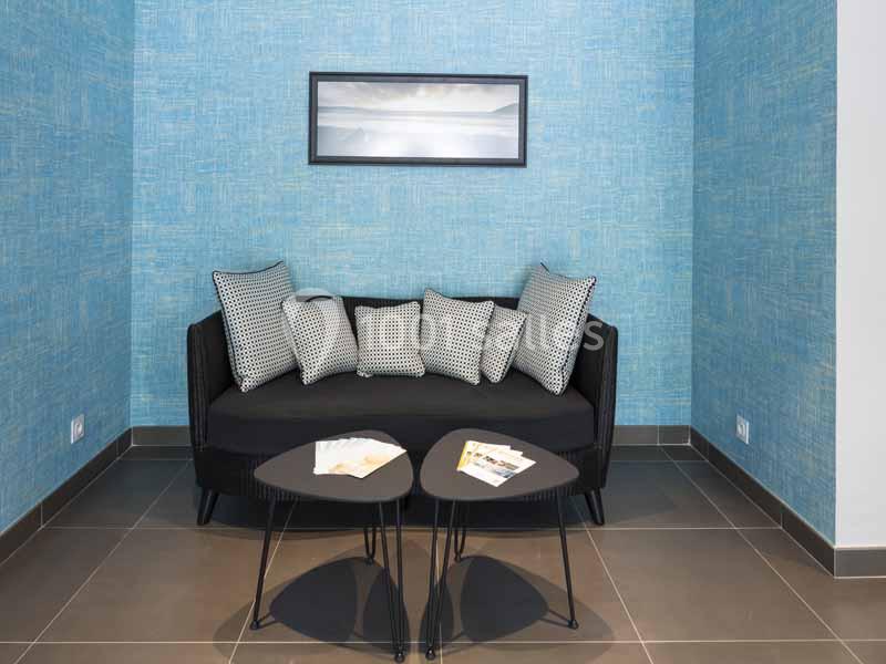 Canapé noir avec coussins à motifs géométriques, tables basses noires et mur bleu texturé en arrière-plan.