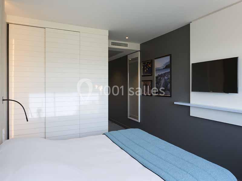 Chambre moderne avec lit, armoire blanche, mur gris, télévision murale et décorations murales.