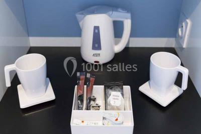 Quatre fauteuils noirs avec coussins clairs entourent une table basse dans une pièce décorée de cadres et luminaires…