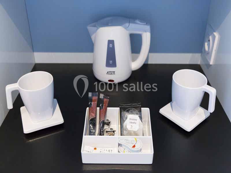 Bouilloire électrique blanche avec deux tasses sur soucoupes et un plateau contenant des sachets de boissons.