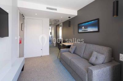 Quatre fauteuils noirs avec coussins clairs entourent une table basse dans une pièce décorée de cadres et luminaires…