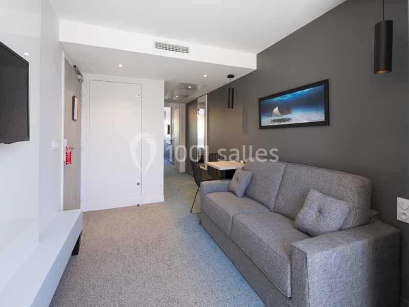 Salon moderne avec canapé gris, table à manger, mur gris décoré d'un tableau, et éclairage encastré.