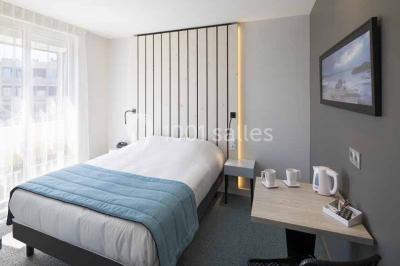 Quatre fauteuils noirs avec coussins clairs entourent une table basse dans une pièce décorée de cadres et luminaires…