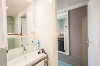 Quatre fauteuils noirs avec coussins clairs entourent une table basse dans une pièce décorée de cadres et luminaires…