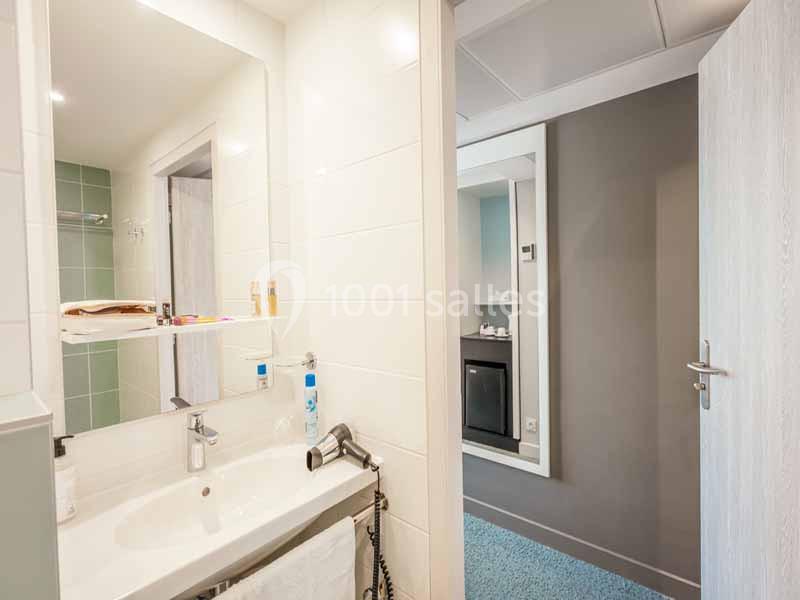 Salle de bain moderne avec lavabo, miroir, sèche-cheveux et vue partielle sur une chambre adjacente.