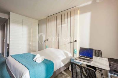 Quatre fauteuils noirs avec coussins clairs entourent une table basse dans une pièce décorée de cadres et luminaires…