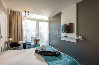 Quatre fauteuils noirs avec coussins clairs entourent une table basse dans une pièce décorée de cadres et luminaires…