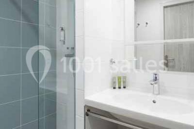 Quatre fauteuils noirs avec coussins clairs entourent une table basse dans une pièce décorée de cadres et luminaires…