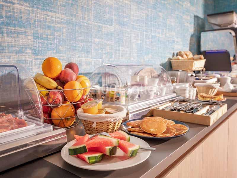Buffet de petit-déjeuner avec fruits frais, pancakes, pain et condiments sur un comptoir dans un cadre lumineux.