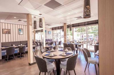 Quatre fauteuils noirs avec coussins clairs entourent une table basse dans une pièce décorée de cadres et luminaires…