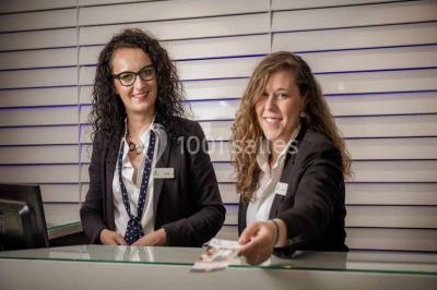 Quatre fauteuils noirs avec coussins clairs entourent une table basse dans une pièce décorée de cadres et luminaires…