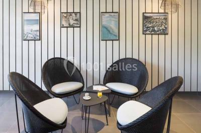 Quatre fauteuils noirs avec coussins clairs entourent une table basse dans une pièce décorée de cadres et luminaires…