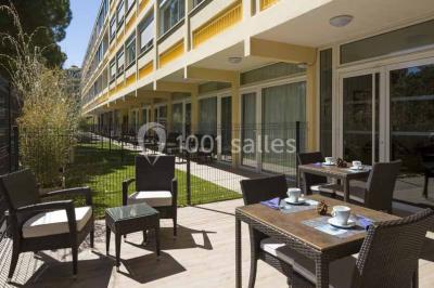 Quatre fauteuils noirs avec coussins clairs entourent une table basse dans une pièce décorée de cadres et luminaires…