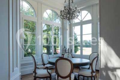 Commode rouge surmontée de cadres, lampe noire et carafe, avec un mur en pierre en arrière-plan.