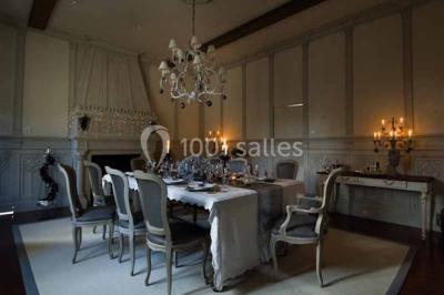 Commode rouge surmontée de cadres, lampe noire et carafe, avec un mur en pierre en arrière-plan.