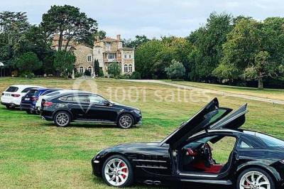 Commode rouge surmontée de cadres, lampe noire et carafe, avec un mur en pierre en arrière-plan.