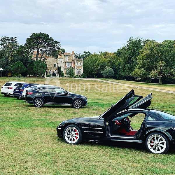 Voitures de luxe garées sur une pelouse devant un grand bâtiment ancien entouré d'arbres.