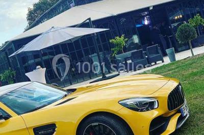 Commode rouge surmontée de cadres, lampe noire et carafe, avec un mur en pierre en arrière-plan.