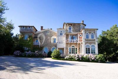 Commode rouge surmontée de cadres, lampe noire et carafe, avec un mur en pierre en arrière-plan.